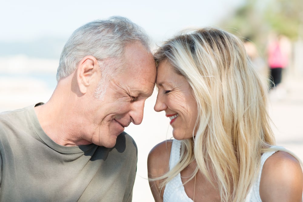 Loving middle-aged couple touching foreheads and smiling happily as they spend a relaxing day at the beach